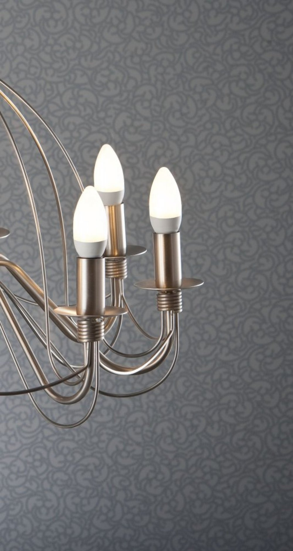 Lampadario con tre lampadine accese. Apparecchio d'argento. Sfondo grigio. Primo piano del lampadario.