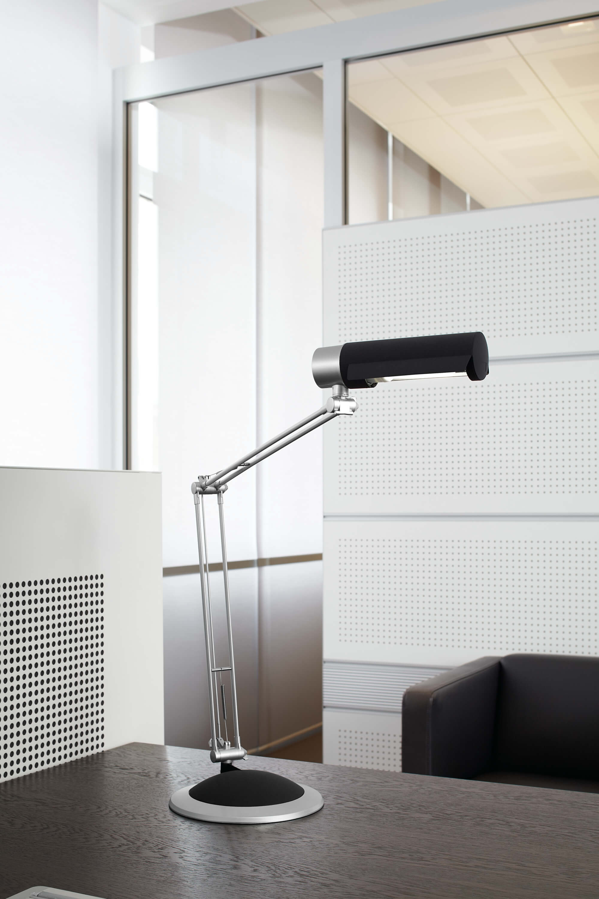 Lampa biurkowa z czarnym kloszem i srebrnym ramieniem na drewnianym biurku.