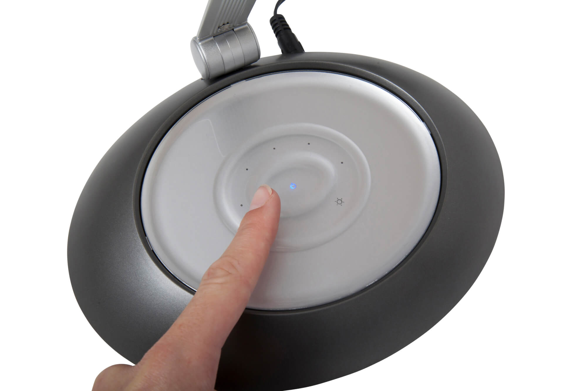 Dłoń naciskająca przycisk na szarej podstawie lampy, białe tło, zbliżenie, podświetlona niebieska kropka.