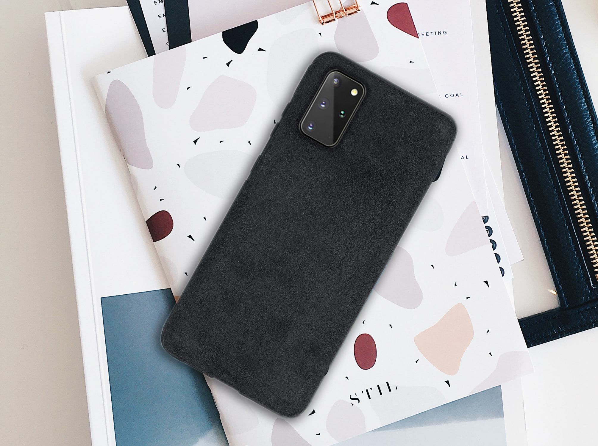 Ein schwarzes Telefon mit schwarzer Hülle auf einem Notizbuch. Die Hülle ist dunkel und bedeckt das Telefon.