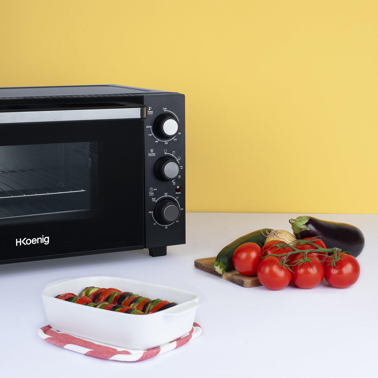 Forno con verdure e ratatouille cotto su tavolo bianco, sfondo giallo.