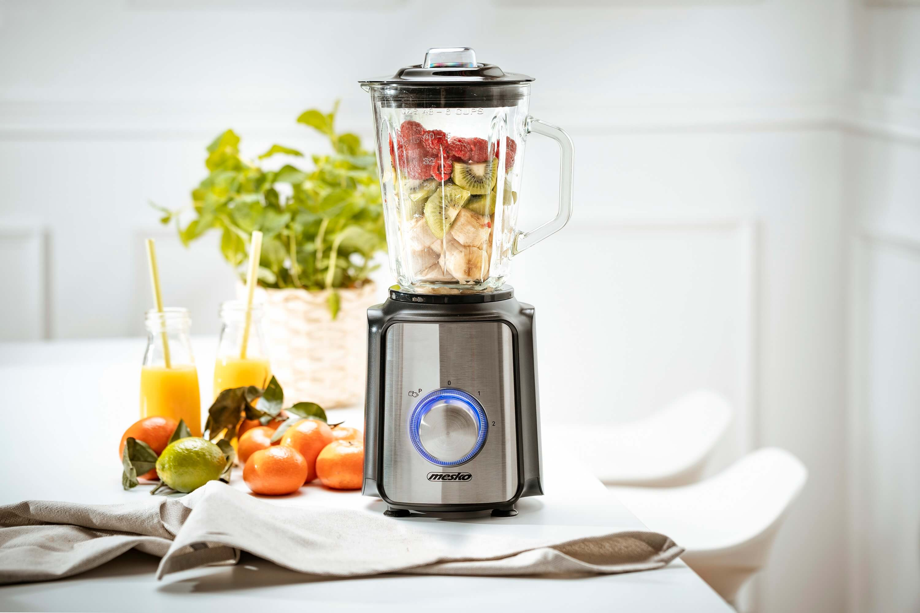 Blender wypełniony owocami, z owocami i napojami na stole.