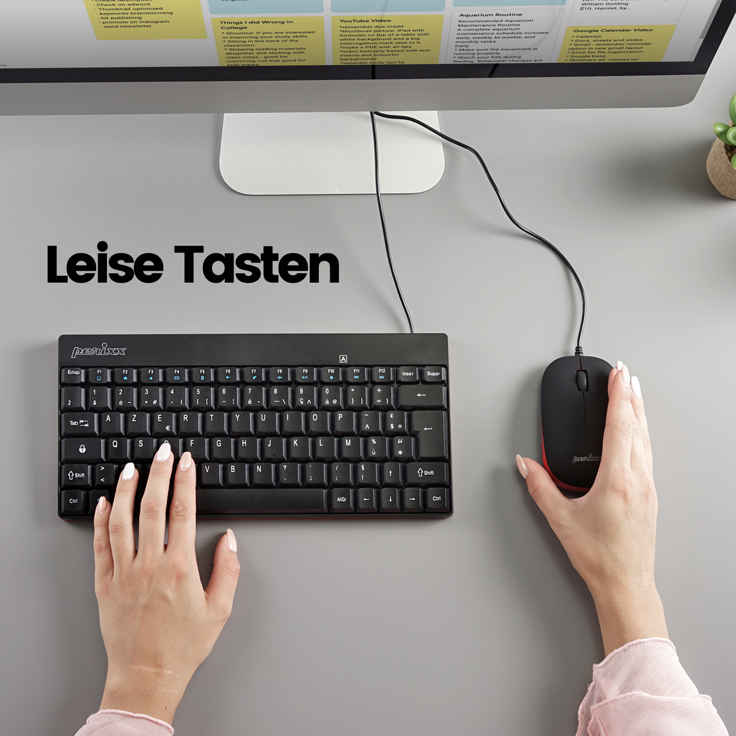 Hände tippen auf einer schwarzen Tastatur mit einer rot akzentuierten Maus auf einem grauen Schreibtisch.