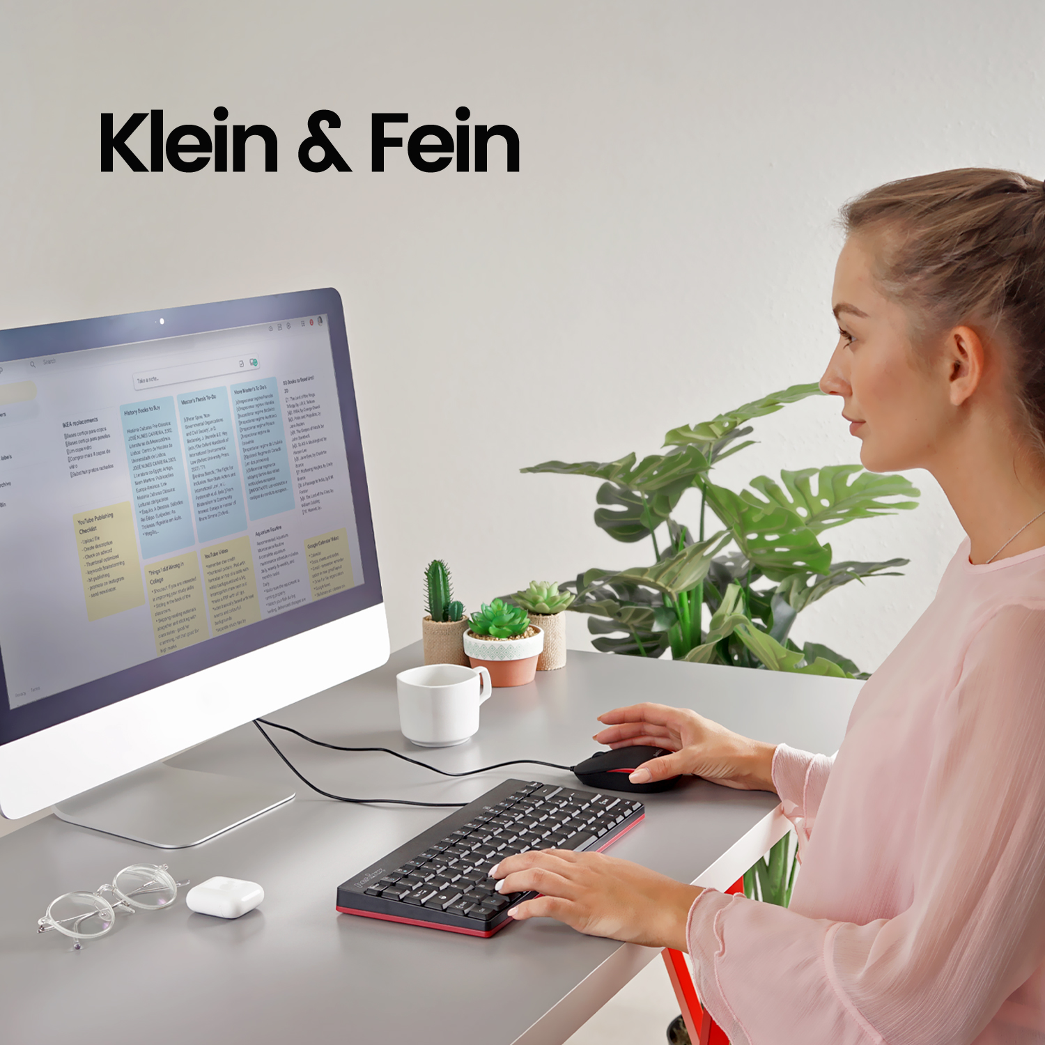 Eine Frau arbeitet an einem Schreibtisch mit einem Computer. Auf dem Schreibtisch liegen Gläser, eine Tasse und Pflanzen.