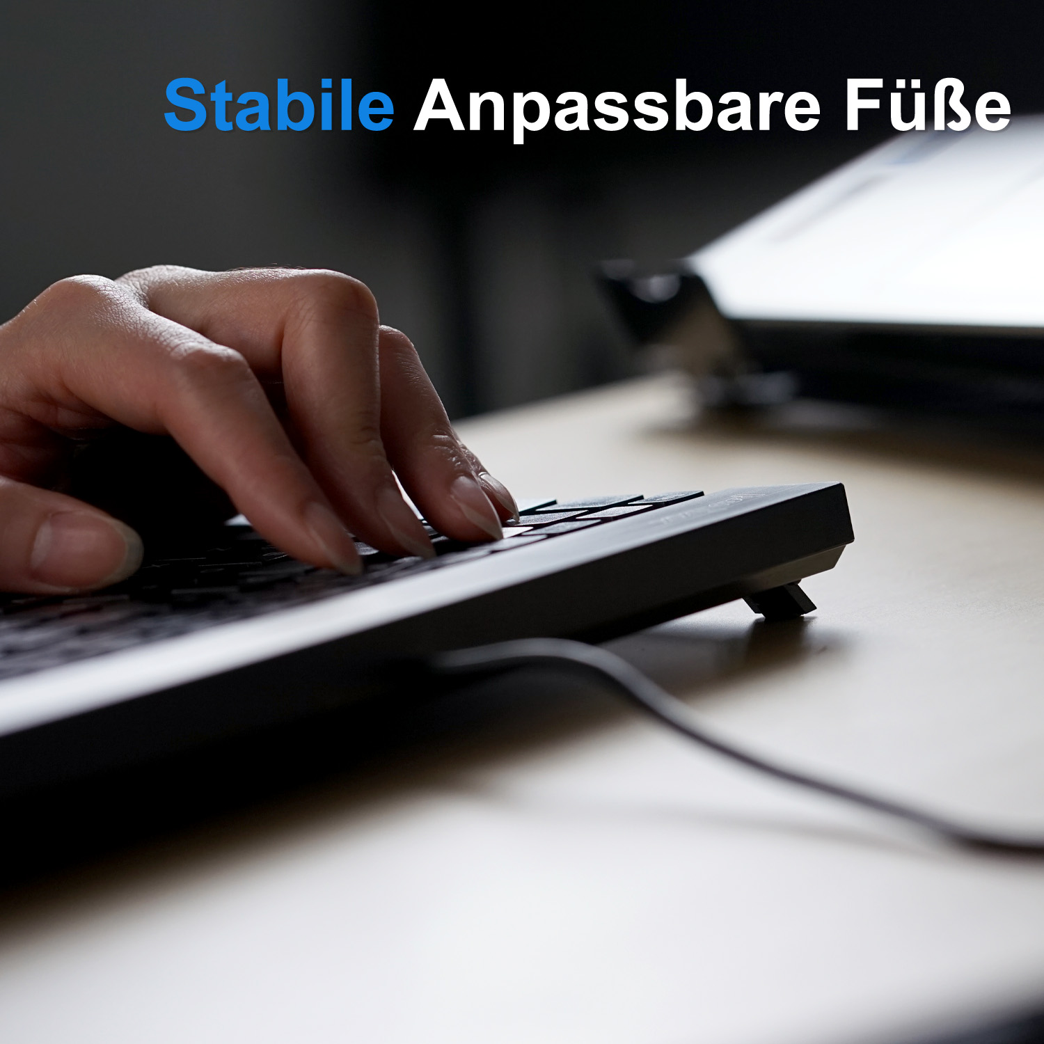 Person tippt auf einer schwarzen Tastatur auf einem Holzschreibtisch. Der Text 'Stabile Anpassbare Füße' ist sichtbar.