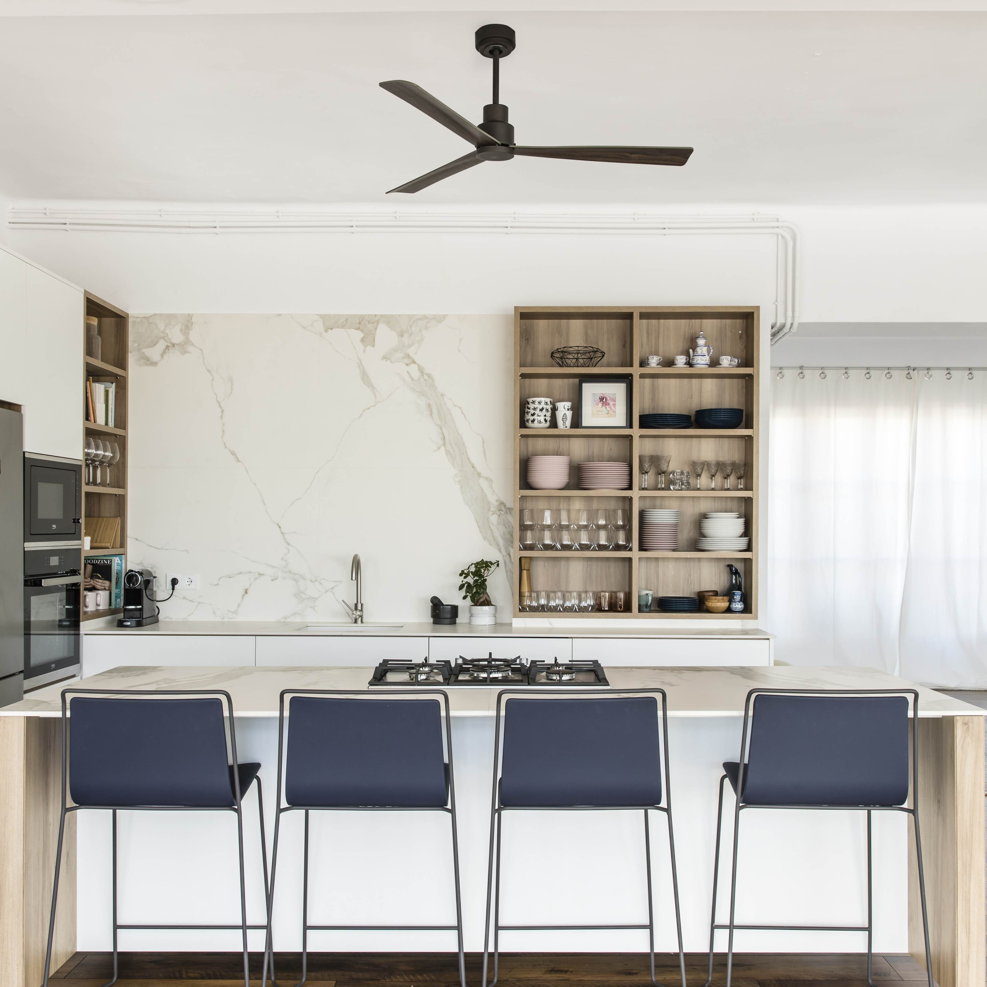 Cucina moderna con mobili bianchi, alzatina in marmo, isola con sedie e ventilatore a soffitto.
