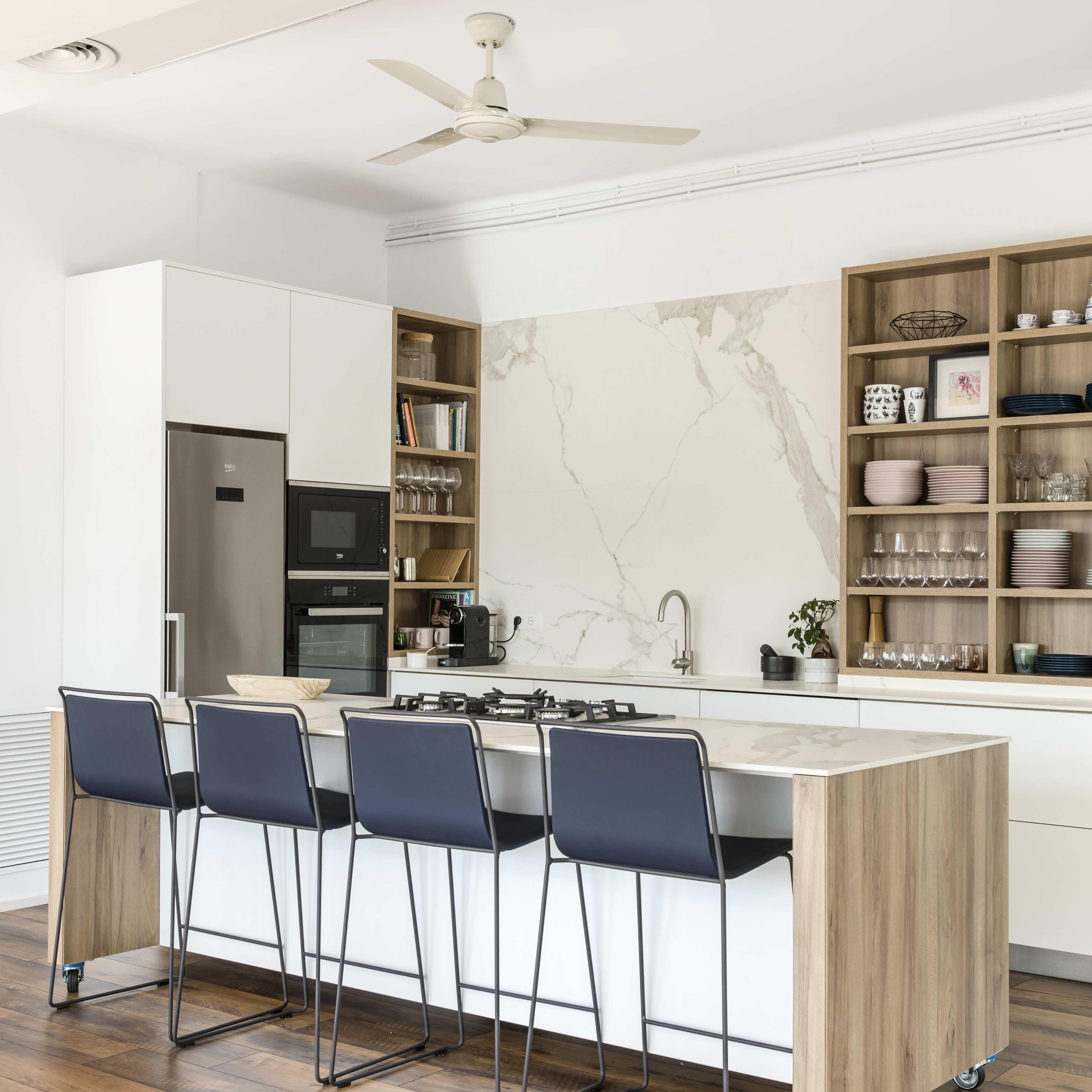Cucina moderna con isola, sgabelli e elettrodomestici in acciaio inox. Mobili in legno e bianchi.