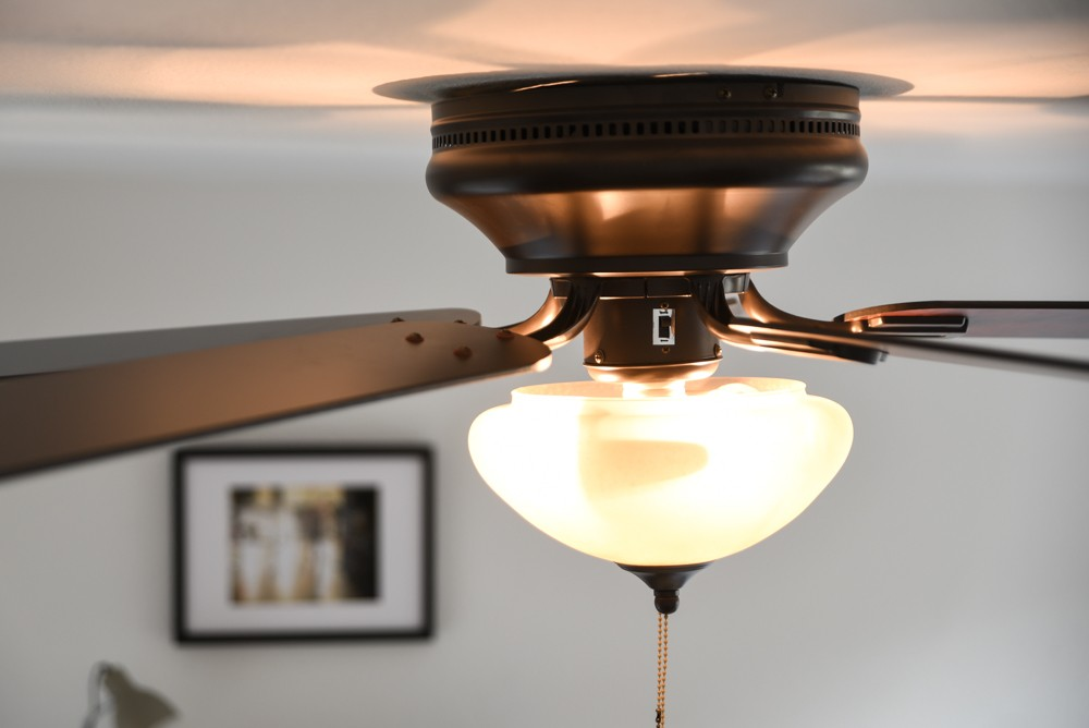 Ein Deckenventilator mit einer Leuchte. Der Ventilator ist dunkel mit einer weißen Kugelleuchte.