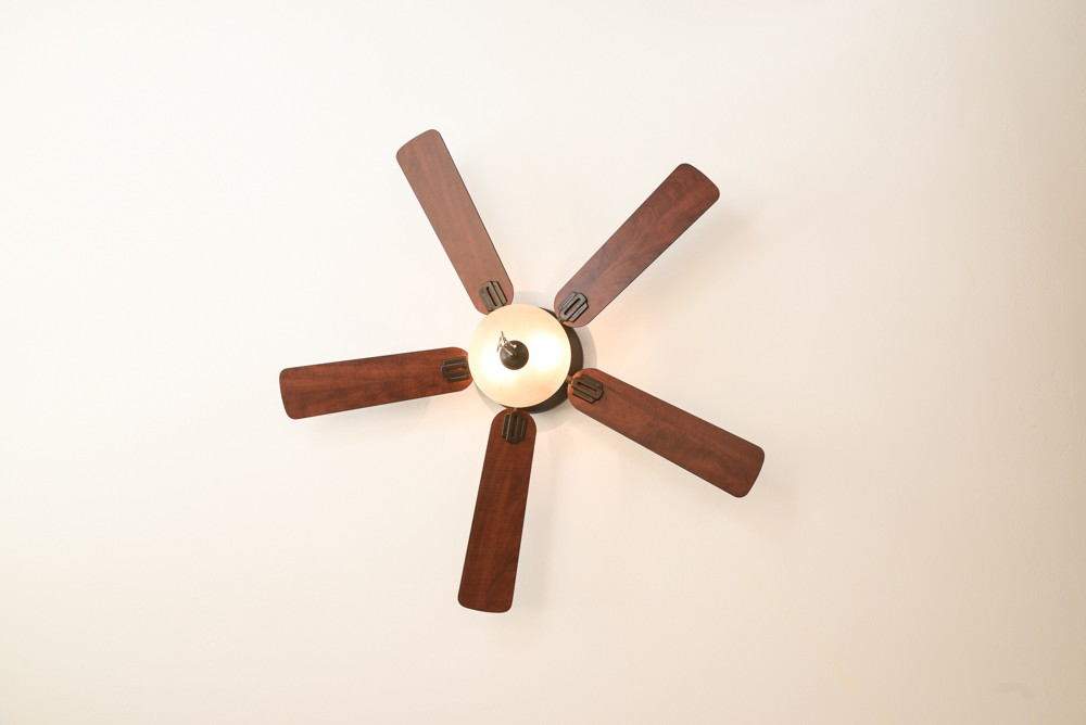 Deckenventilator mit fünf Holzflügeln. Weißer Deckenhintergrund.