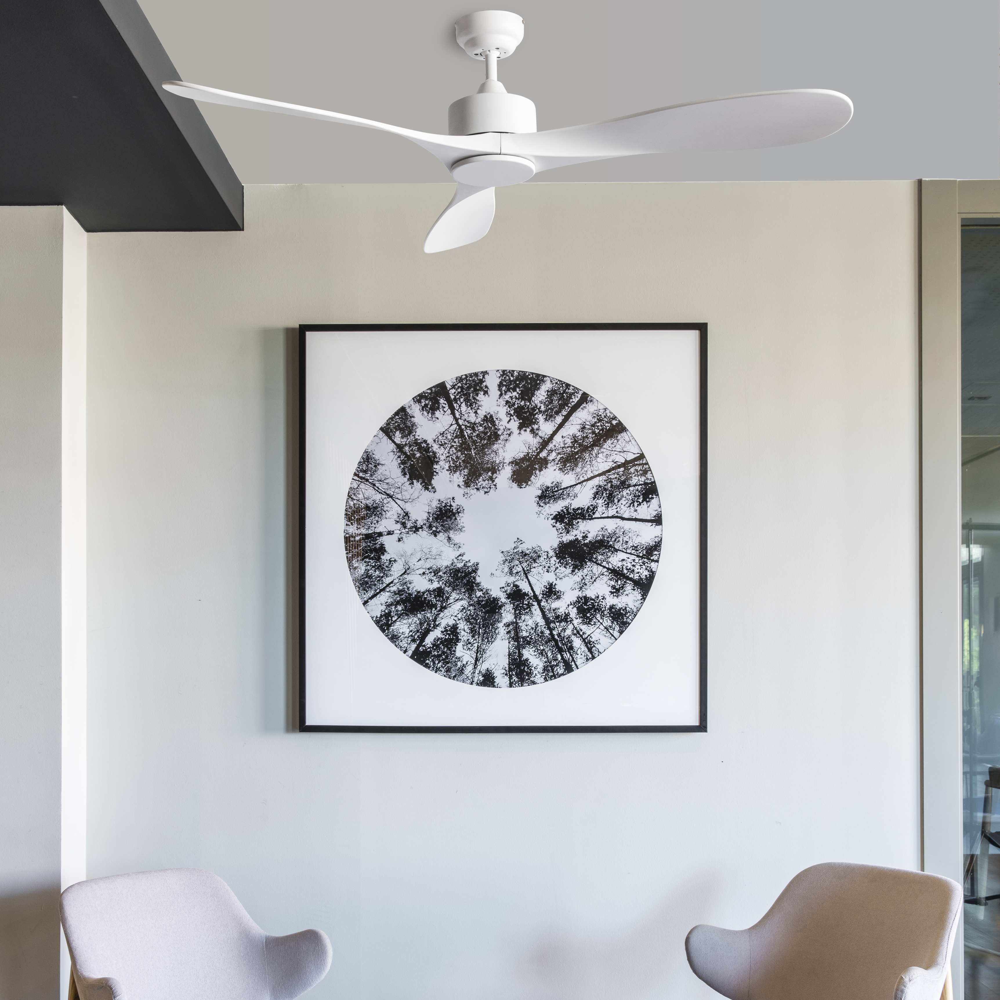 Weißer Deckenventilator mit drei Flügeln über einem gerahmten Waldbild und zwei Stühlen.