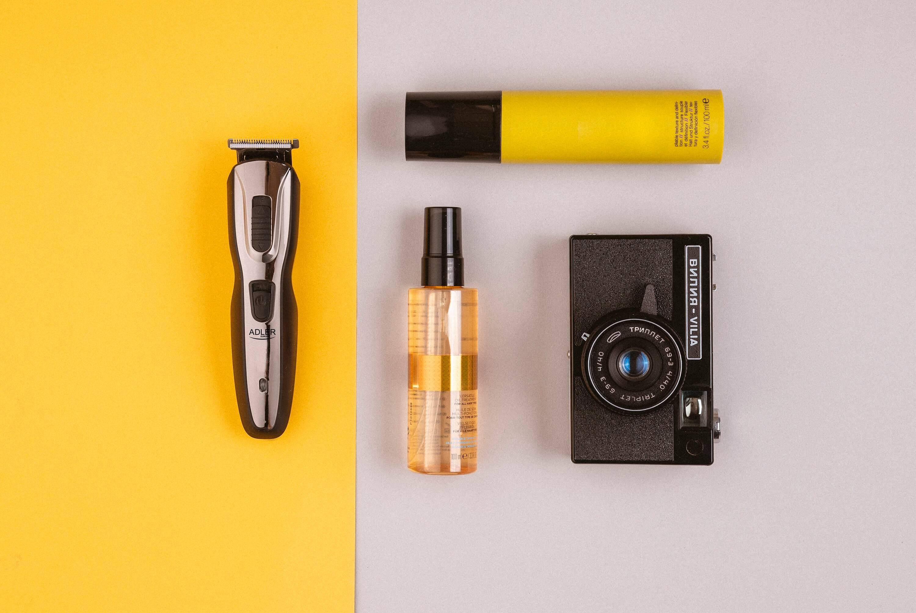 Objekte auf gelber und grauer Oberfläche: Trimmer, Parfümflasche, Kamera. Draufsicht.