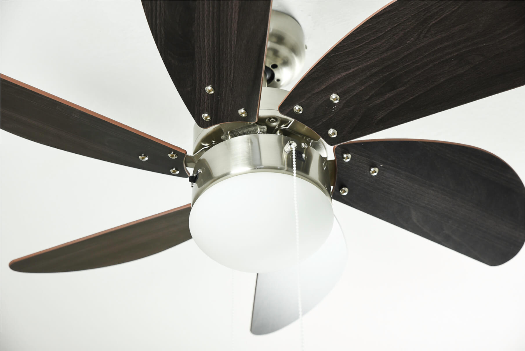 Ein Deckenventilator mit dunkelbraunen Flügeln und einer weißen Leuchte ist an einer weißen Decke montiert.