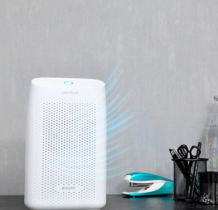 Biały osuszacz powietrza na stole z artykułami biurowymi i szarą ścianą w tle.