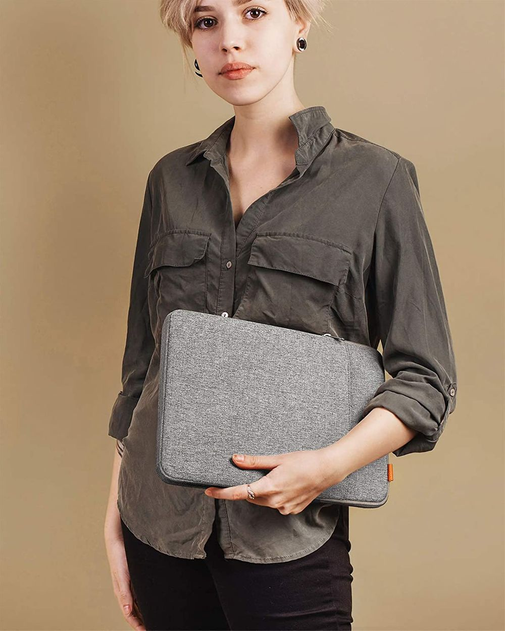 Mujer sosteniendo una funda gris para portátil. Lleva una camisa verde, fondo claro.