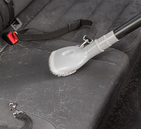 Ein grauer Staubsaugerkopf entfernt Haare von einem Autositz. Schwarzer Sitz mit Haaren.