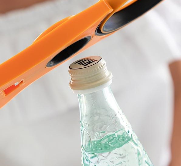 Orange Schere schneidet Flasche. Flasche mit weißem Deckel, klares Glas. Weißer Hintergrund.