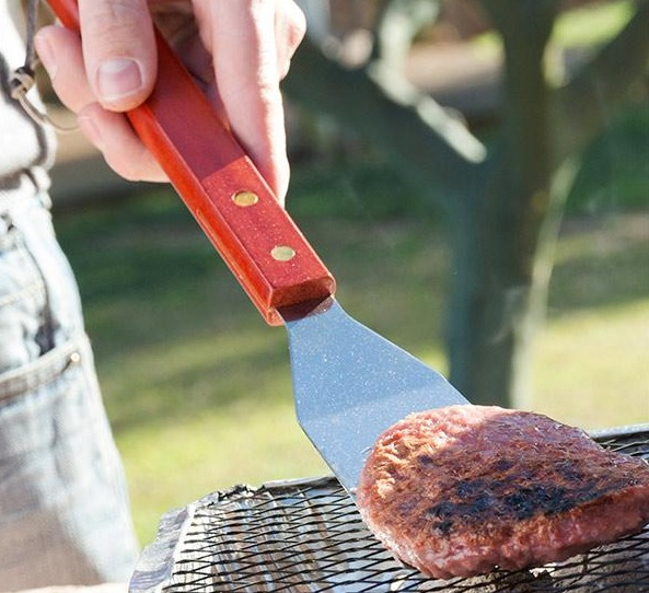 Eine Person grillt einen Burger auf einem Grill. Szene im Freien.