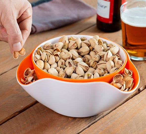 Un cuenco de pistachos con una mano alcanzando para tomar.