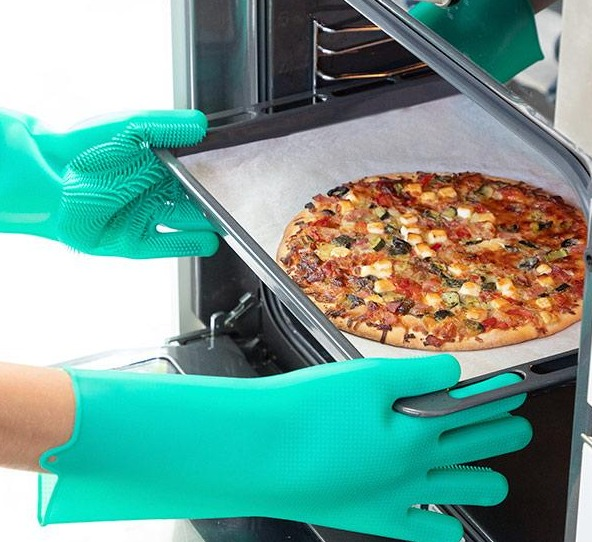 Hände mit grünen Ofenhandschuhen, die eine Pizza aus einem offenen Ofen nehmen, Pizza im Fokus.