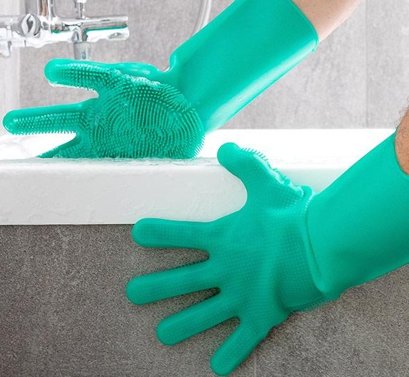 Zwei grüne Silikonhandschuhe mit Scheuerbürsten. Einer in einem Waschbecken mit Seife.