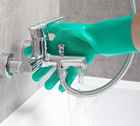 Person reinigt verchromte Armatur mit grünem Handschuh. Wasser fließt.