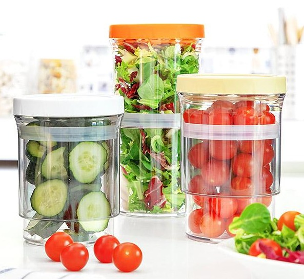 Tre contenitori trasparenti con cetrioli, insalata e pomodori all'interno, con coperchi e basi.