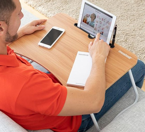 Un uomo usa un tavolino per laptop sulle sue ginocchia. Un telefono e un tablet.