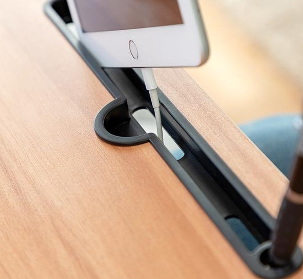 Tablet in carica su scrivania in legno, cavo inserito. Scanalatura nera tiene cavo e tablet.