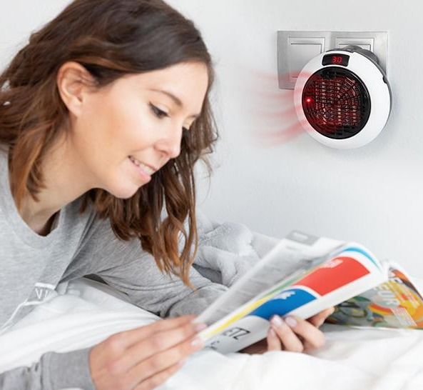 Donna che legge una rivista a letto. Un piccolo riscaldatore è collegato al muro.