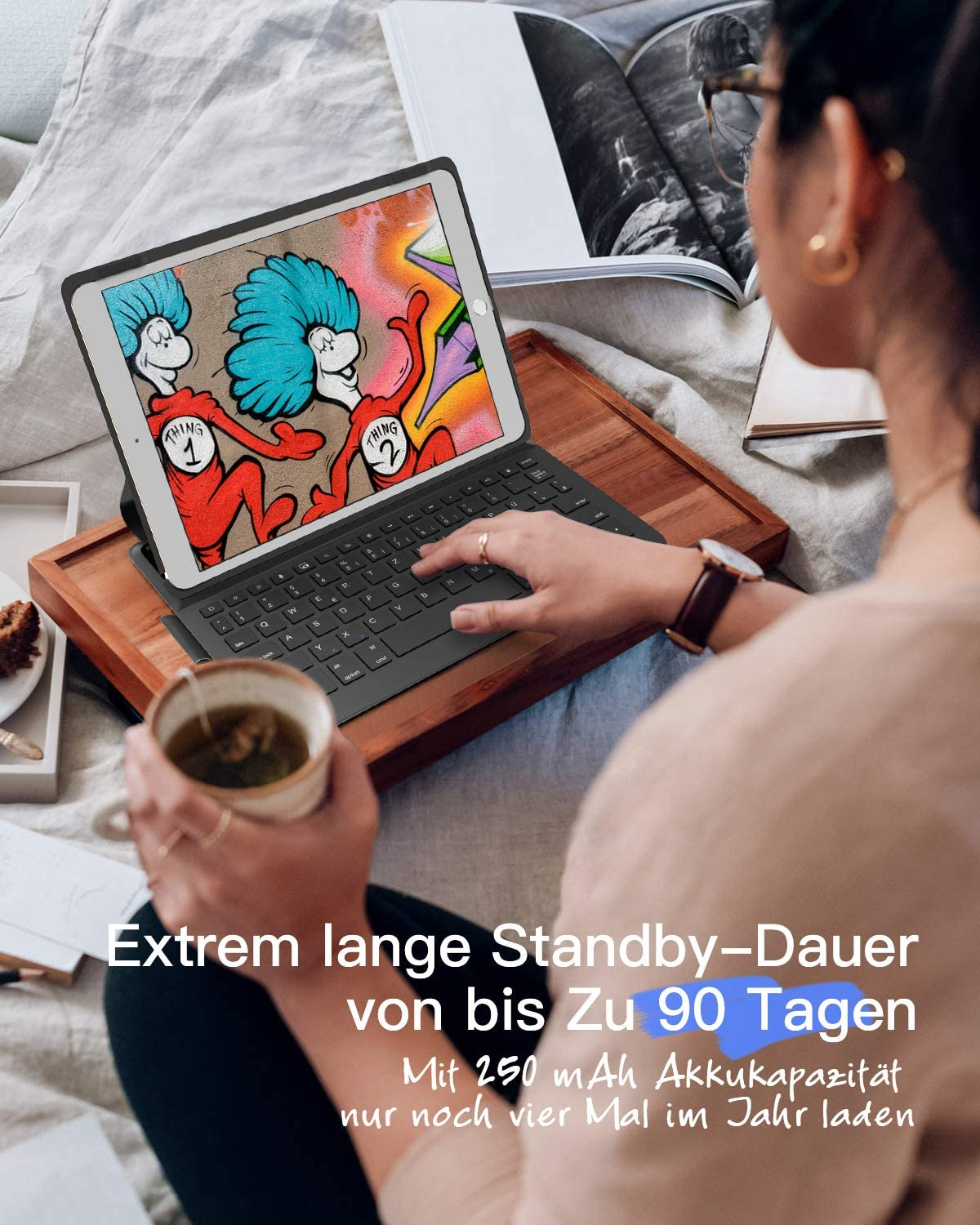 Frau benutzt Tablet mit Tastatur auf einem Bett. Sie hält eine Teetasse. Bettwäsche im Hintergrund.
