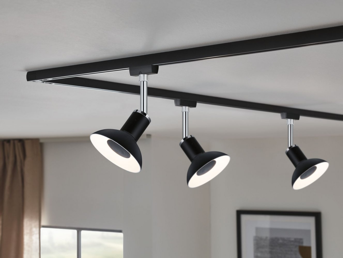 Drei schwarze Strahler, die von einer schwarzen Schiene an einer weißen Decke hängen, mit einem dunklen Rahmen.