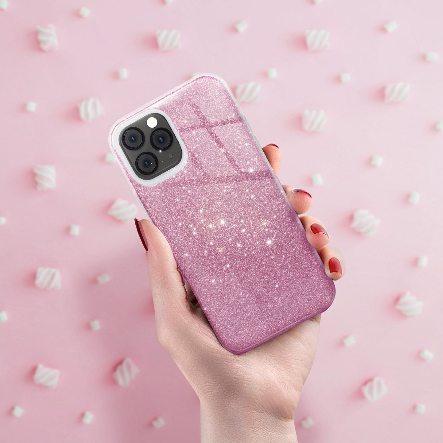 Hand hält eine pinke Glitzer-Handyhülle mit Kameraausbuchtung, Marshmallows im Hintergrund.