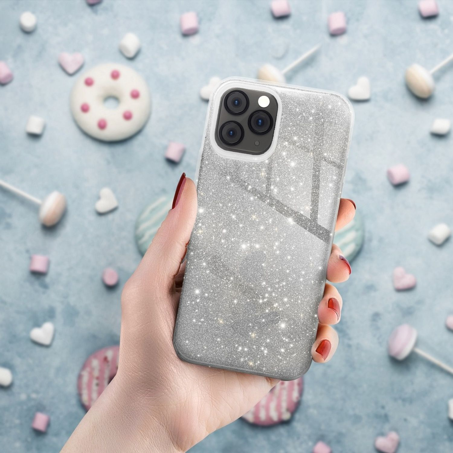 Hand, die eine glitzernde Handyhülle hält, mit verschwommenem Hintergrund mit Süßigkeiten.
