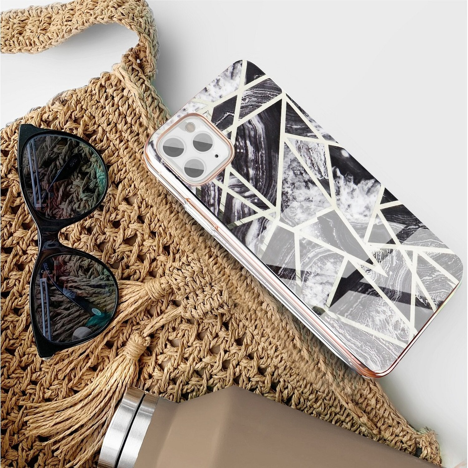 Eine Tasche, Sonnenbrille und eine Handyhülle mit Marmordesign liegen auf einer weißen Oberfläche.