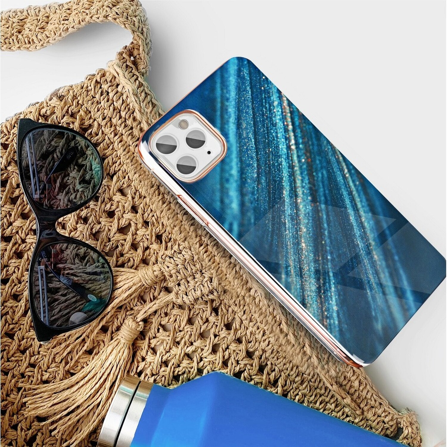Handyhülle mit blauem Streifendesign, die auf einer Tasche und Sonnenbrille liegt.