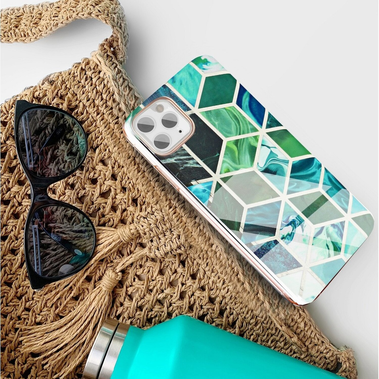 Tasche mit Sonnenbrille, Telefon und Wasserflasche. Telefon hat geometrisches Design in Grün und Weiß.