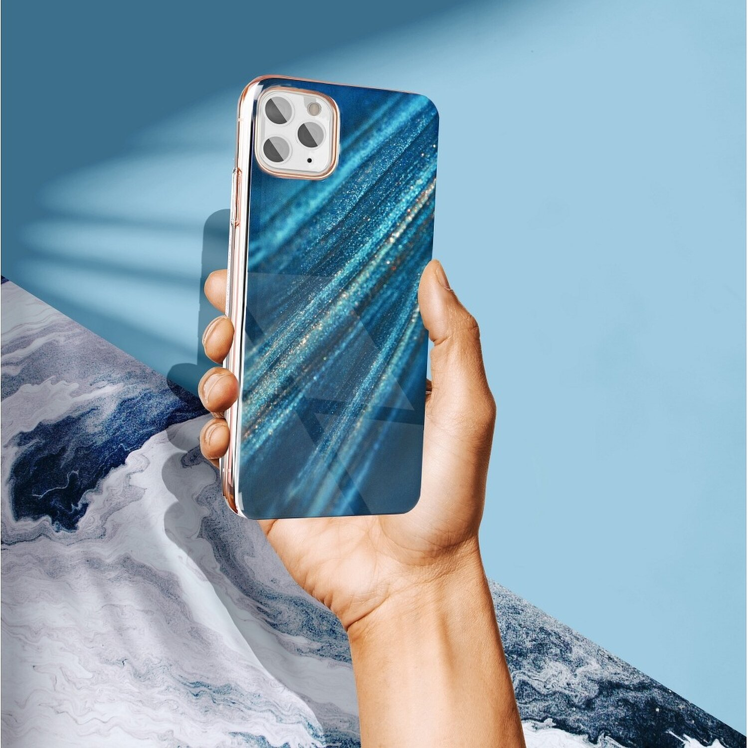 Eine Hand, die eine Smartphone-Hülle mit blauem und goldenem Design hält, vor blau-weißem Hintergrund.