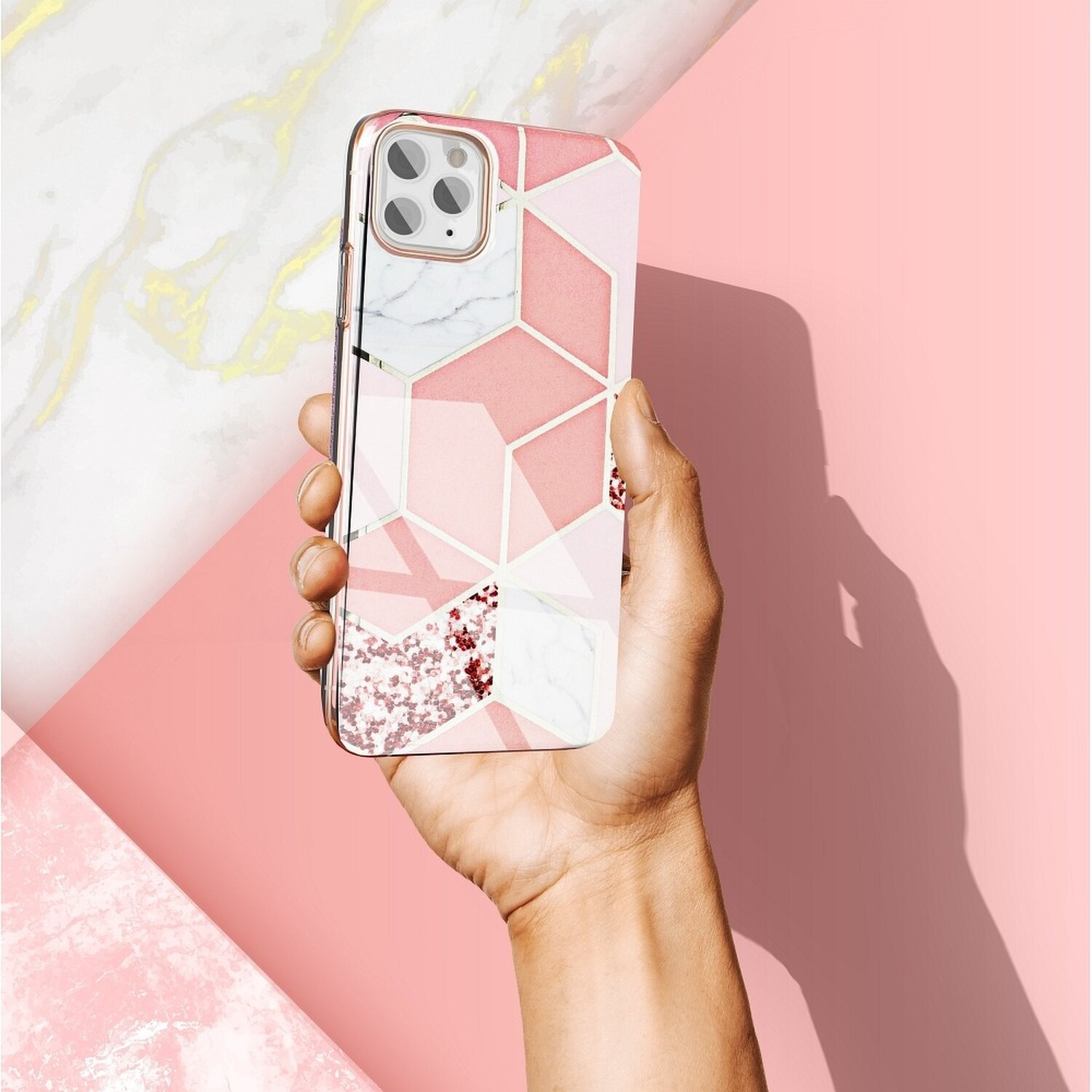 Eine Hand, die eine Handyhülle mit einem rosa-weißen geometrischen Design hält. Rosa Hintergrund.