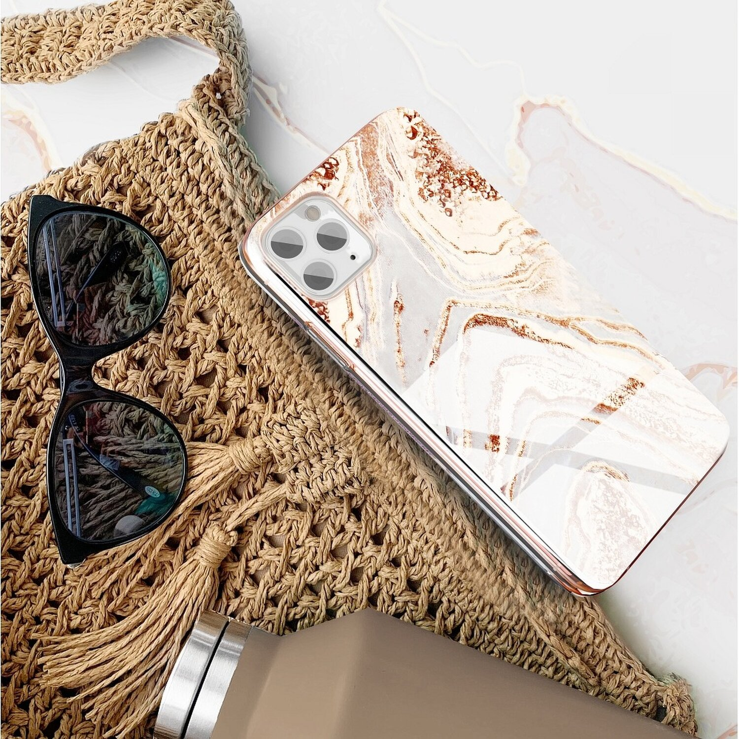 Telefon mit Marmorgehäuse, Sonnenbrille und Tasche auf Marmoroberfläche.