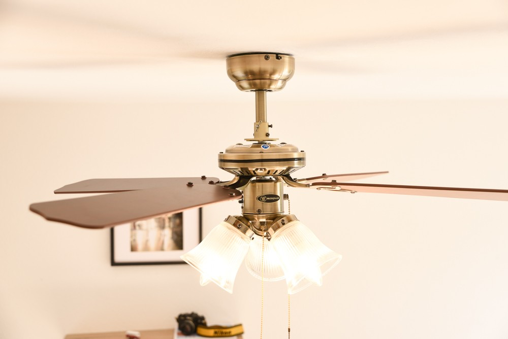 Ventilatore a soffitto con tre pale e luci. Oro e marrone con luci sotto.