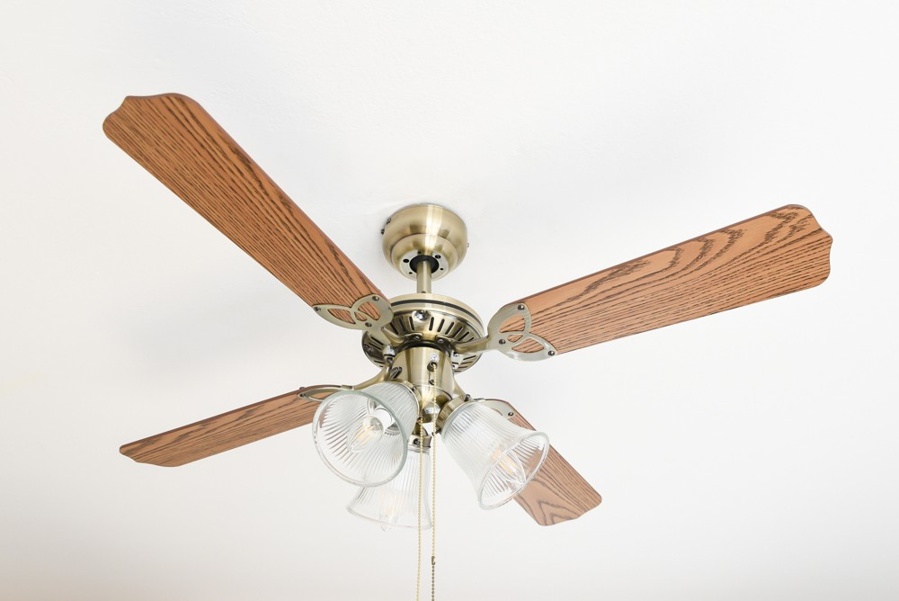 Ventilatore a soffitto con quattro pale in legno e tre lampade in vetro.