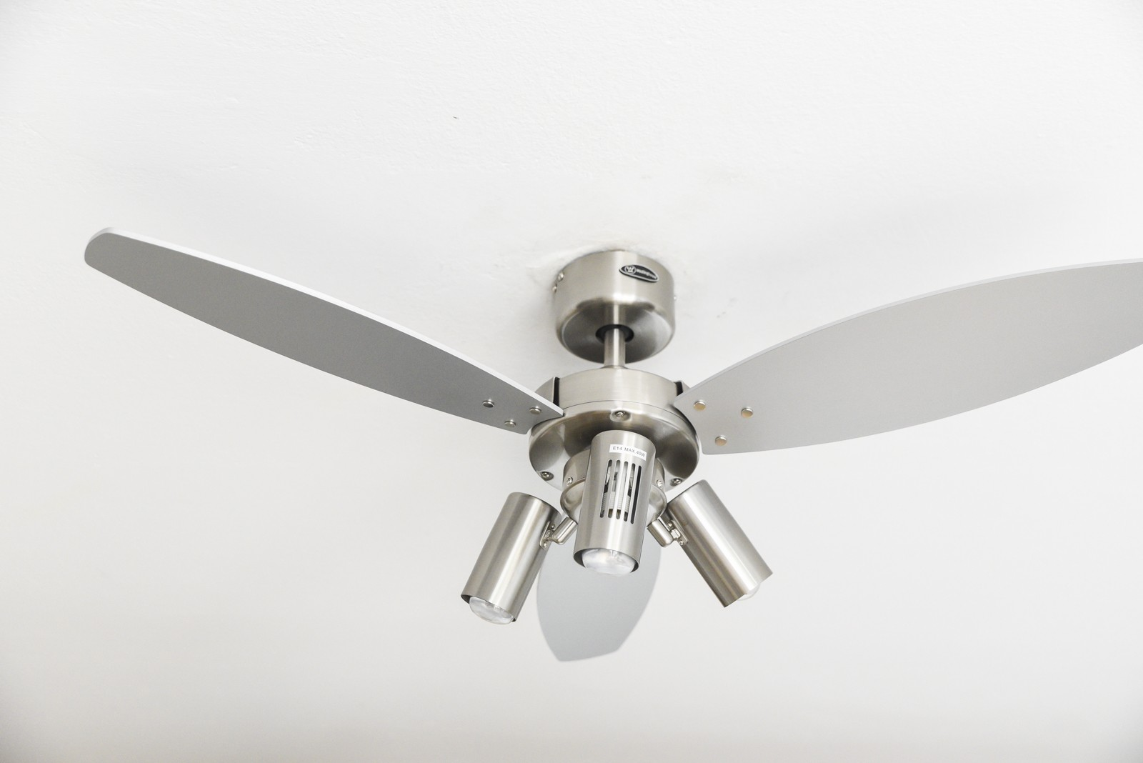 Silberner Deckenventilator mit drei Lichtern, an weißer Decke montiert, ein schlichtes Design.