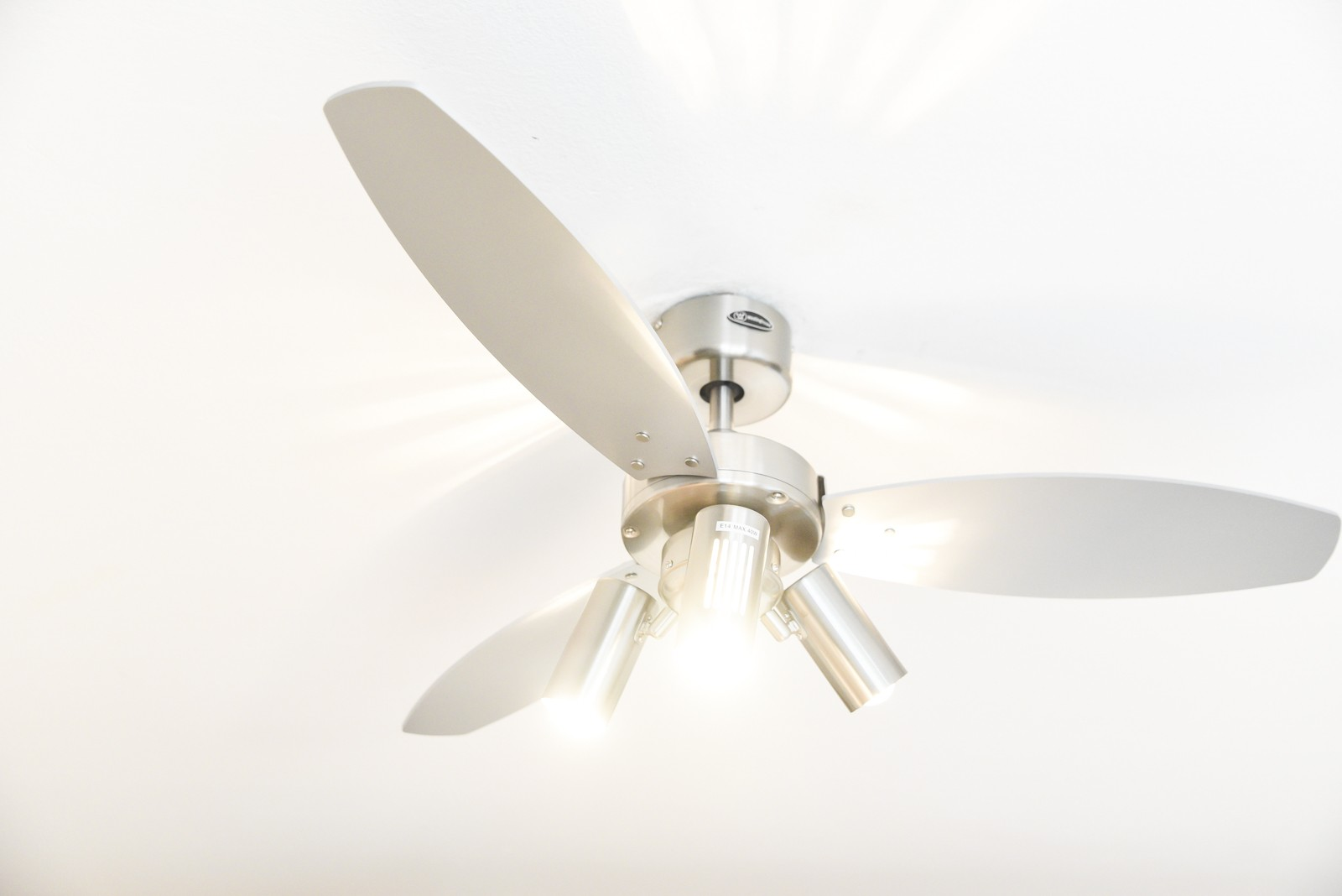 Deckenventilator mit drei Flügeln und drei Lichtern, weißer Hintergrund.