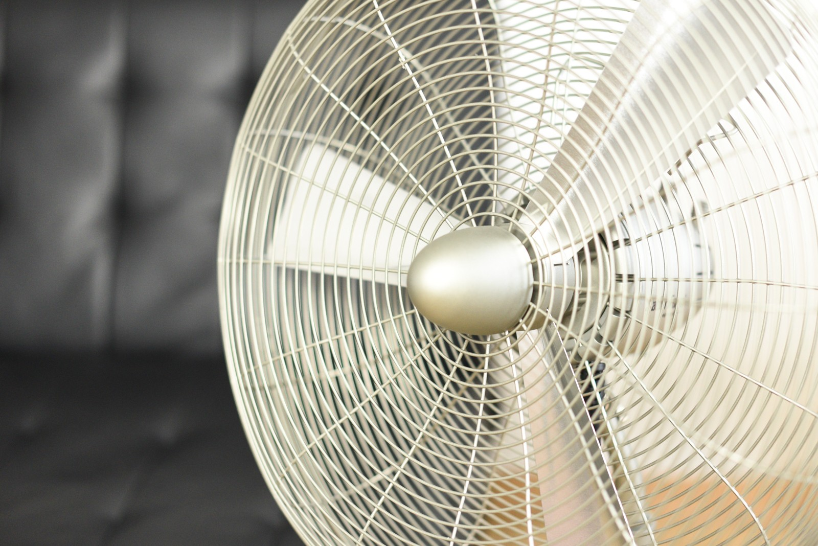 Gros plan d'un ventilateur argenté avec un fond noir matelassé flou.
