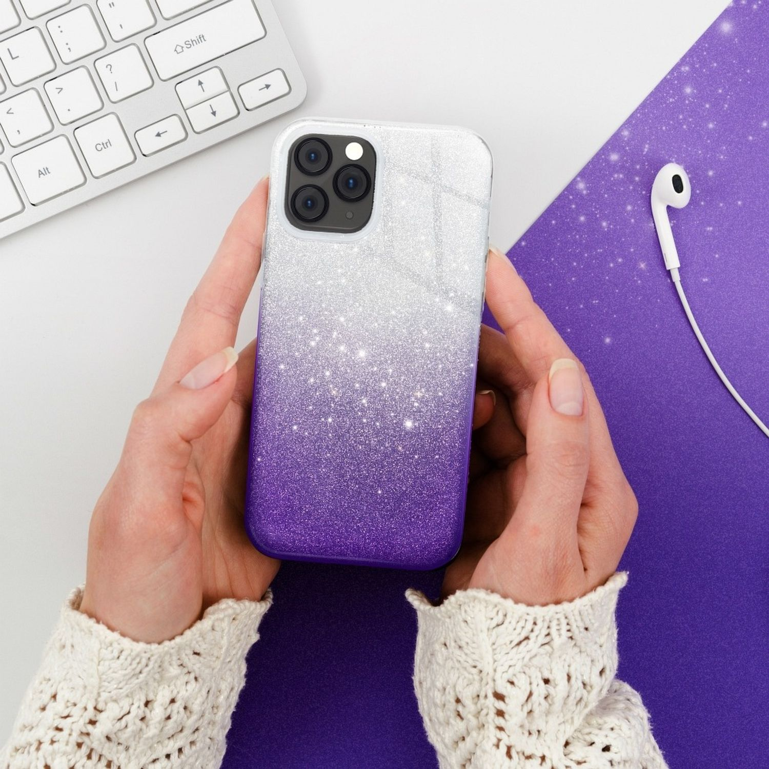 Eine Person hält ein Telefon mit einer lila und weißen Glitzerhülle. Es gibt weiße Kopfhörer.