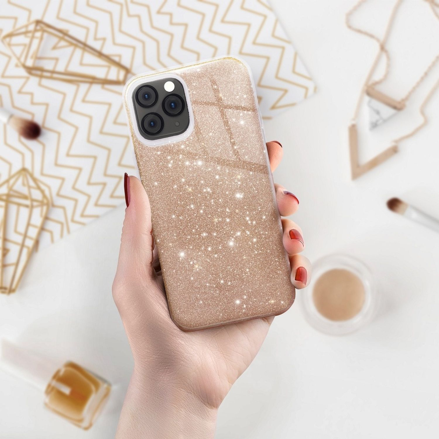 Hand hält glitzernde Handyhülle, Make-up-Artikel im Hintergrund.