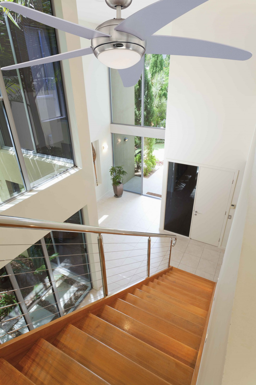 Draufsicht auf ein helles Interieur mit Treppe, Deckenventilator und großen Fenstern.
