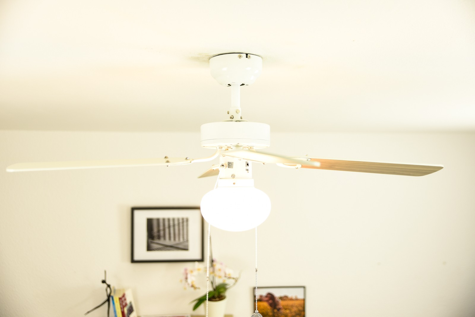 Weißer Deckenventilator mit drei Flügeln und Licht, unter einer weißen Decke, mit Dekorationen.
