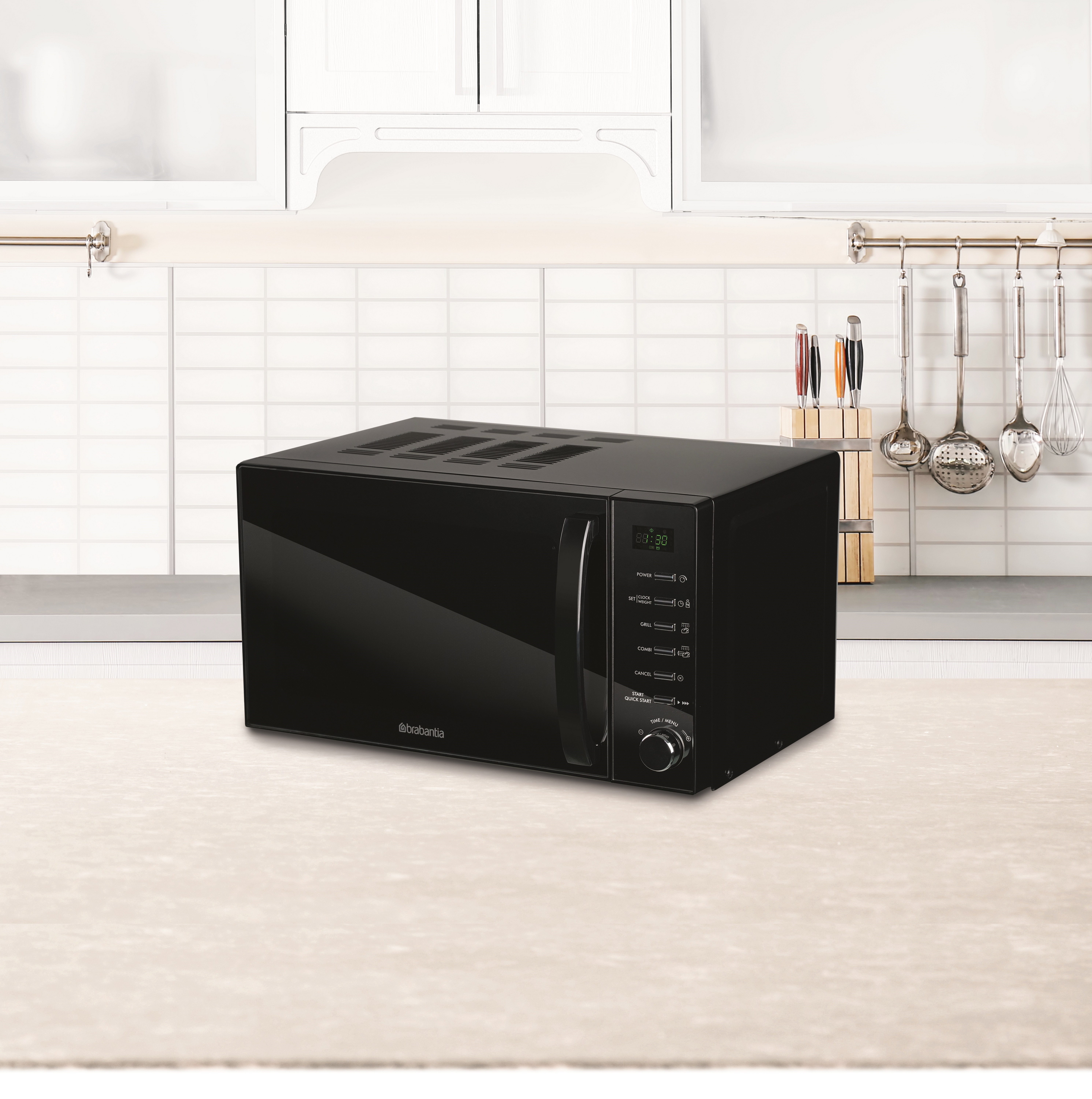Black microwave oven on a light-colored countertop, with a tiled wall and kitchen utensils in the background.