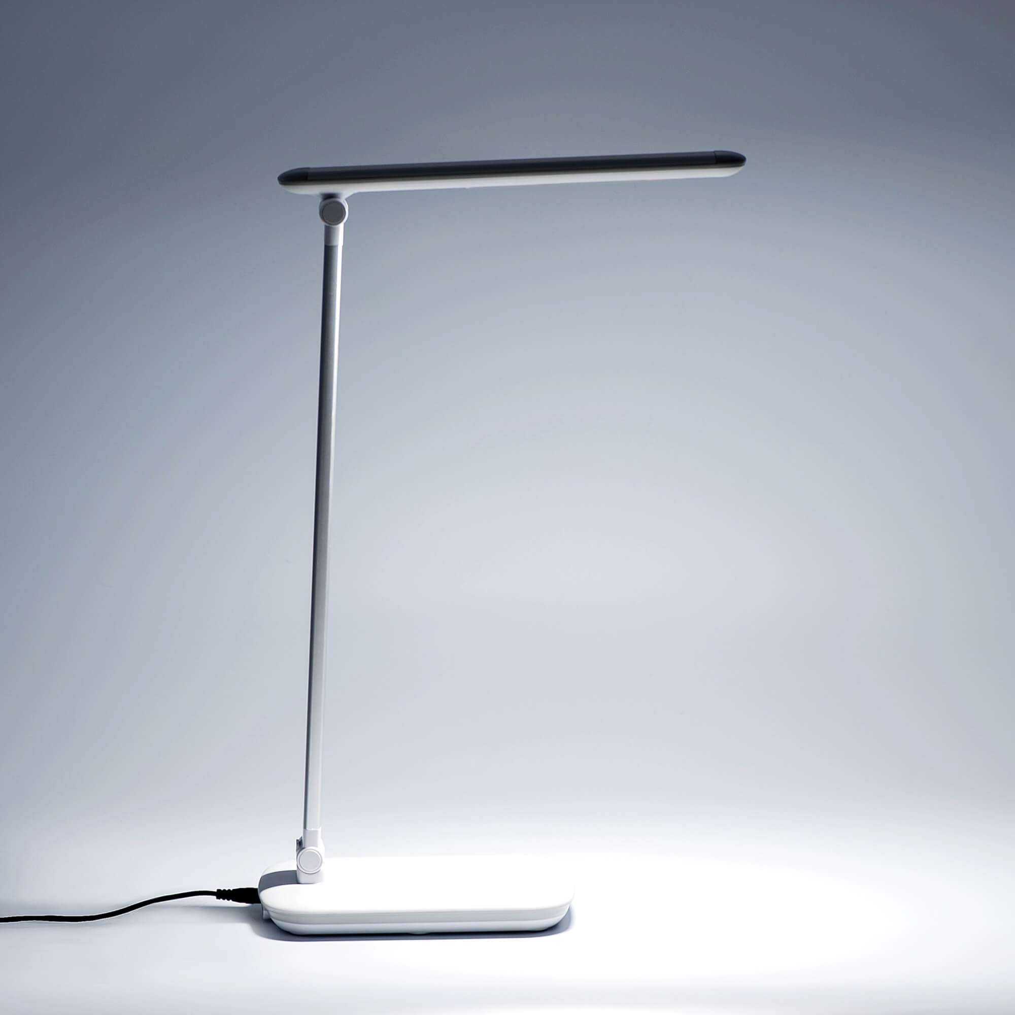 Lampada da scrivania bianca moderna, con supporto alto argentato e barra luminosa orizzontale.